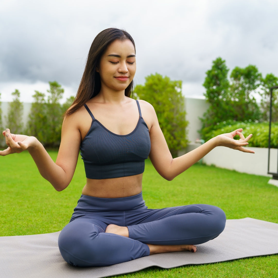 Woman in blue athletic wear practicing yoga outdoors on a grassy area.